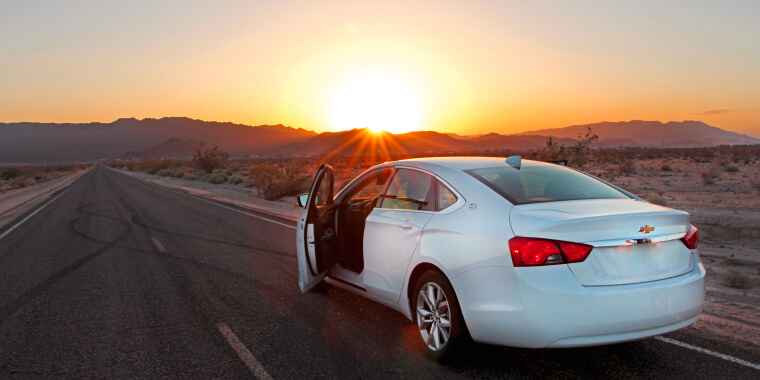 Chevrolet Impala con las puertas abiertas en una autopista al atardecer