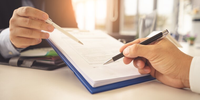 Manos sosteniendo plumas y revisando notas en cuaderno