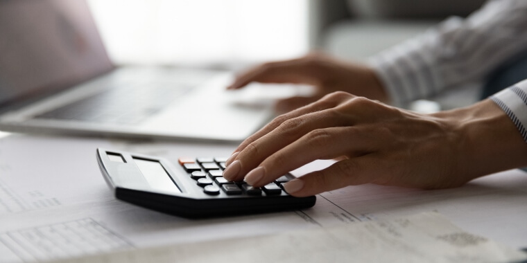 Mujer utilizando una calculadora y con una computadora a un lado