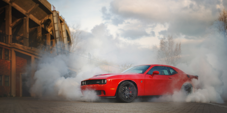 Dodge Challenger color negro estacionado en diagonal con las luces encendidas y echando humo por su alta velocidad