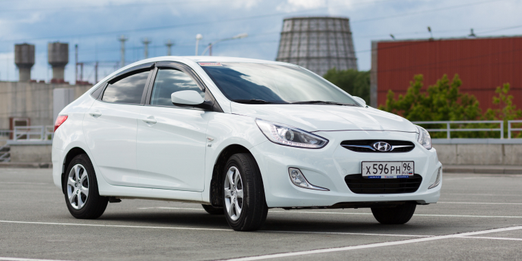 Hyundai Accent blanco estacionado en un centro de venta durante un día nuboso.