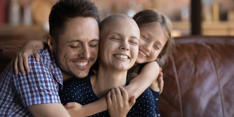 Mujer hispana sin cabello junto a su esposo e hija felices tras vencer su enfermedad y tener un seguro para cáncer.
