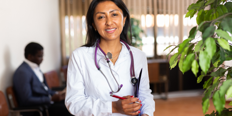 Doctora hispana con su estetoscopio y sosteniendo un folder, lista para atender a los pacientes con seguro médico.