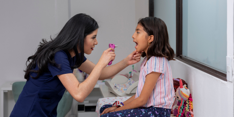Pediatra hispana observa y revisa la boca de una niña en una consulta.