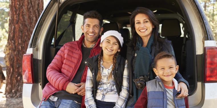 Familia latina sonriendo sobre su vehículo
