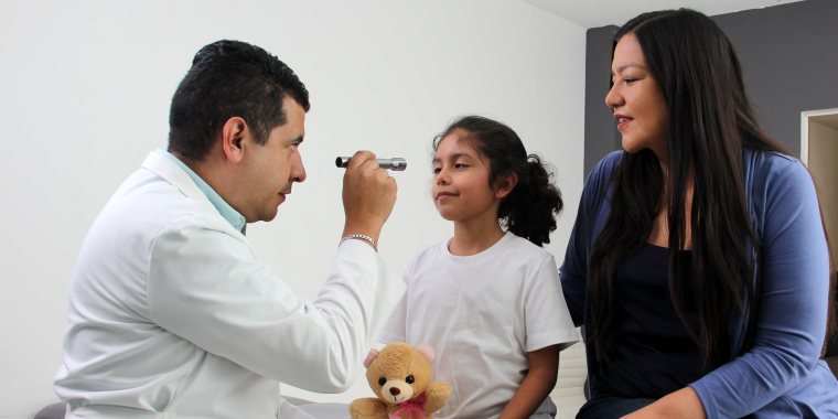 Doctor hispano en consulta del Seguro Médico Medicaid con niña y su madre.