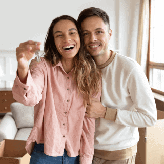 Joven pareja sosteniendo las llaves de su nuevo hogar con un seguro para casa.