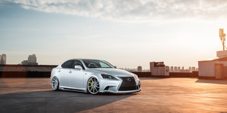 Lexus IS plateado estacionado frente al horizonte de la ciudad.