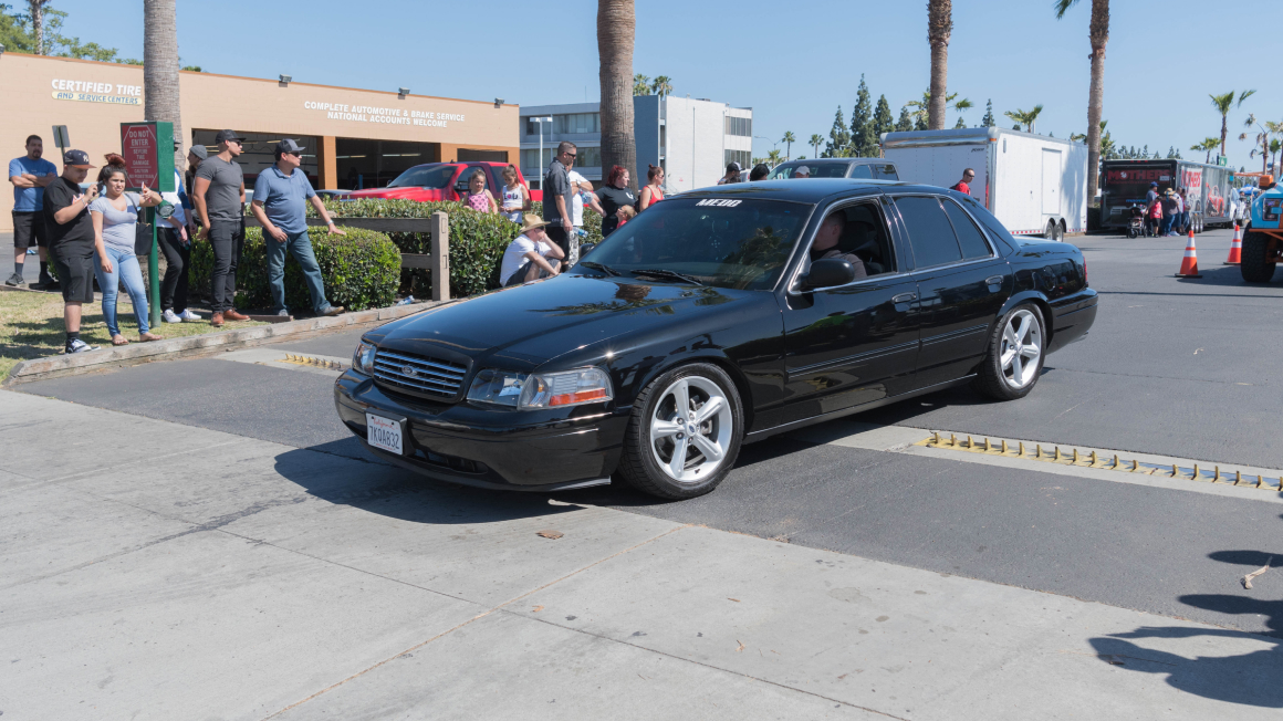 Ford Crown Victoria negro avanzando en la calle durante una exhibición de autos.