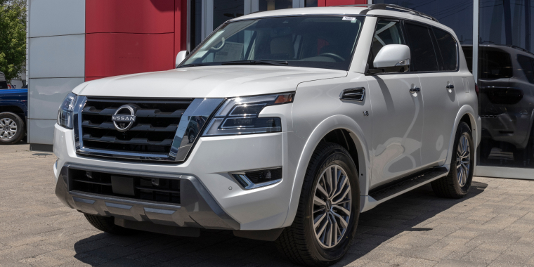 Nissan Armada dorada estacionada frente a una concesionaria de vehículos en un día soleado.