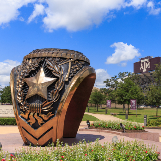 Estatua de anillo en la ciudad de College Station, con estadio de fútbol Kyle Field al fondo. Seguro de auto barato en College Station, Texas.