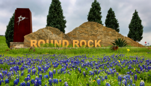 Señal monumental en la entrada a la ciudad rodeada de campo de flores azules. Round Rock, Texas – Freeway, seguro de auto barato en Round Rock, Texas.