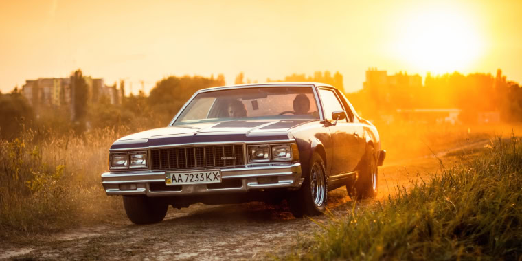 Chevrolet Caprice azul oscuro por una carretera rural al atardecer.