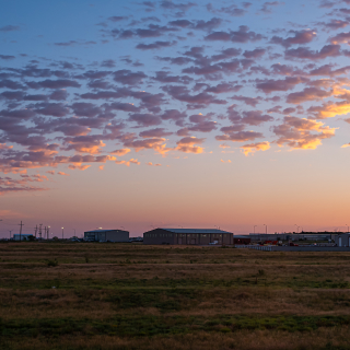 Colorido amanecer oscuro en Snyder Texas con edificio industrial, almacenes o bodegas y la fábrica por campo de cultivo con torres de alta tensión - Snyder, seguro de auto barato en Texas.