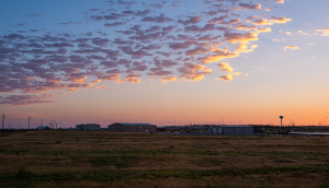 Colorido amanecer oscuro en Snyder Texas con edificio industrial, almacenes o bodegas y la fábrica por campo de cultivo con torres de alta tensión - Snyder, seguro de auto barato en Texas.
