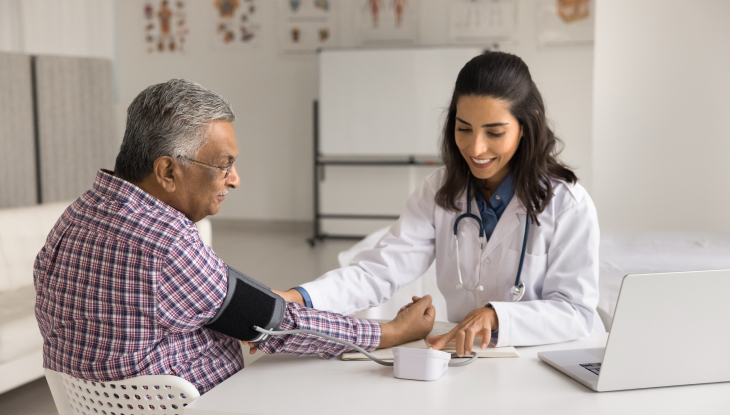 Doctora checando la presión a un anciano hispano que tiene un seguro médico en California.
