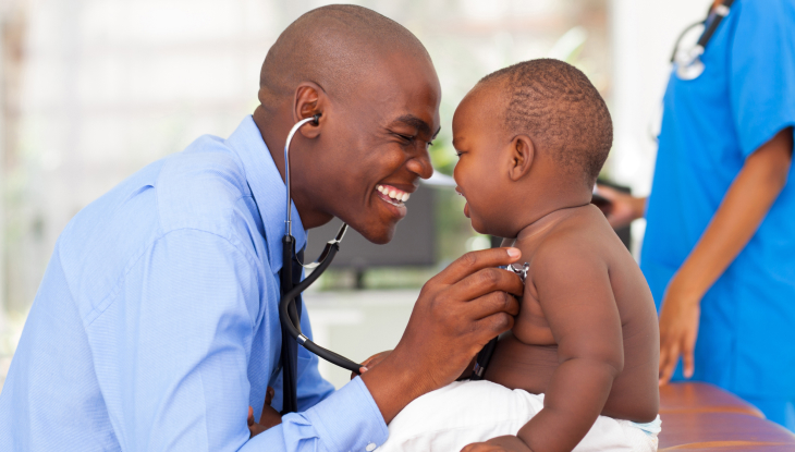 Doctor afroamericano sonriendo mientras revisa el latido del corazón de un bebé. 