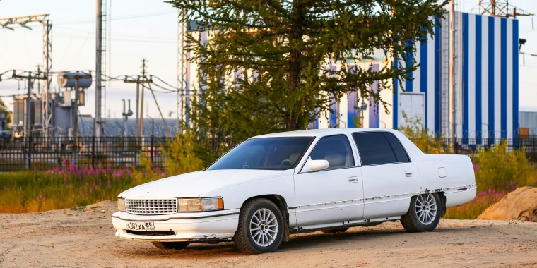 Cadillac DTS sedán blanco con vidrios polarizados avanzando en un camino de tierra durante un día soleado - Seguro de auto barato para Cadillac DTS