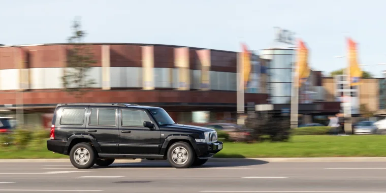 Jeep Commander negra avanzando a velocidad en una carretra asfaltada - Seguro de auto barato para la Jeep Commander