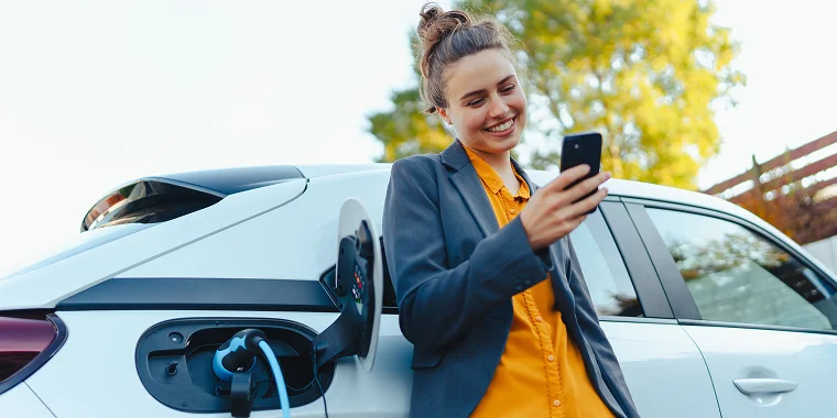 Mujer viendo su celular recostada sobre su vehículo eléctrico