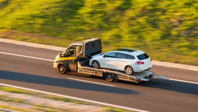 Grúa transportando un auto blanco por carretera, una solución práctica para transportar auto de un estado a otro en Estados Unidos.