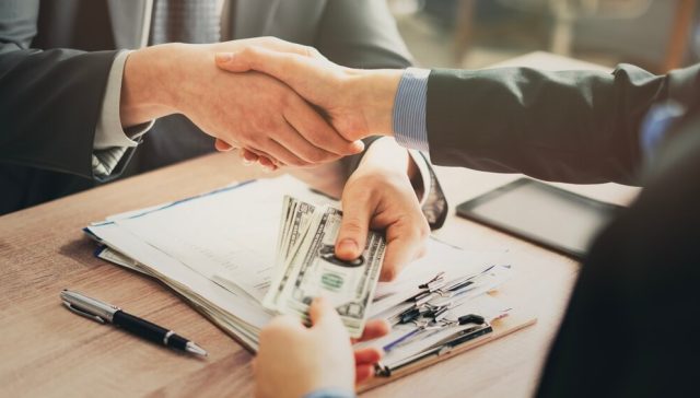 Persona recibiendo dinero mientras firma documentos para obtener un préstamo para autos y financiar la compra de un vehículo.