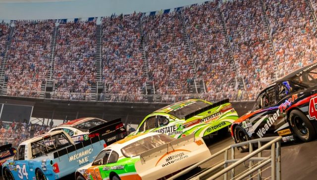 Autos de NASCAR compitiendo frente a una multitud de aficionados en un estadio, mostrando la evolución de los autos de NASCAR y su diseño moderno.