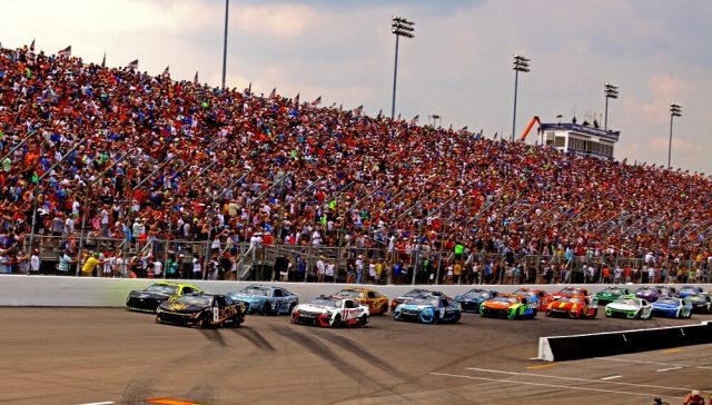 Carrera de NASCAR frente a gradas llenas de aficionados mientras los autos compiten en la pista durante un emocionante evento de automovilismo.