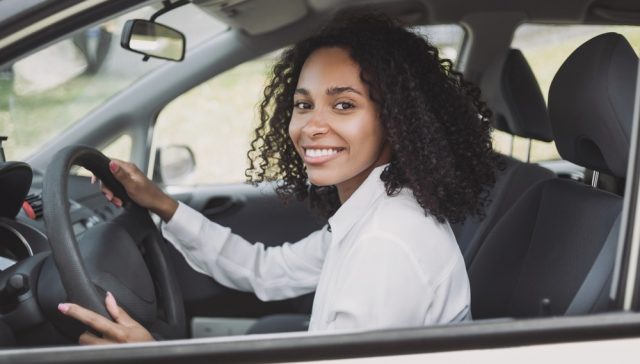 Conductora al volante de su vehículo ante los gastos ocultos de tener un auto en USA