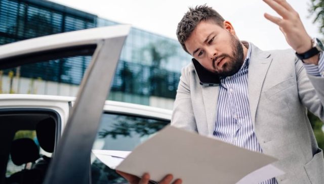 Hombre revisa documentos del vehículo ante posibles señales de alerta al comprar un auto usado.